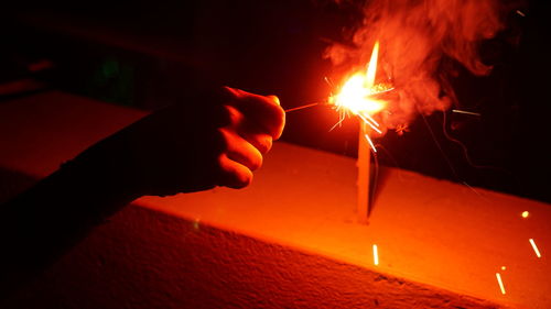 Cropped image of hand holding fire at night