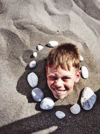 High angle portrait of smiling boy in sand at beach