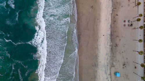 Bird's eye view of sandy beach with palm trees and layered tide