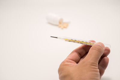 Cropped hand of person holding thermometer against white background