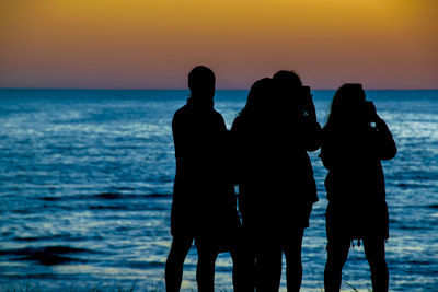 Silhouette people at beach against sky during sunset