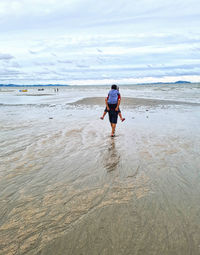 Rear view of woman on beach against sky