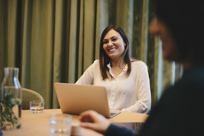 Happy businesswoman sitting wit laptop at conference table in board room