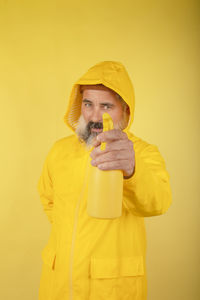Handsome man holding a washing spray in a yellow raincoat standing behind a yellow wall person