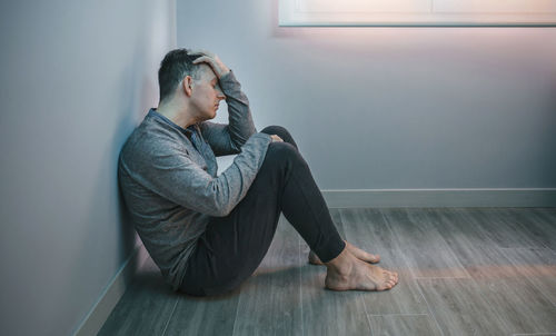 Side view of young woman sitting on hardwood floor at home