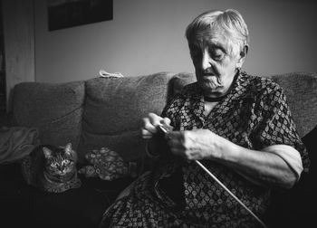 Senior woman knitting wool while sitting with cat on sofa at home