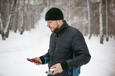 Close-up of man using phone while smoking on snow covered field