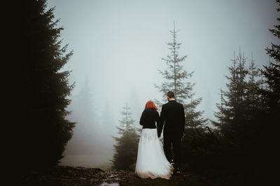 Rear view of bride and bridegroom standing on field