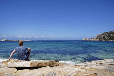 Rear view of man looking at sea against blue sky