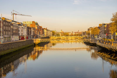 Bridge over river by buildings in city against sky during sunset