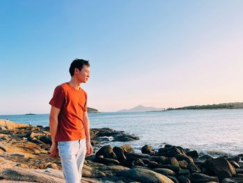 Side view of man standing at beach against clear sky