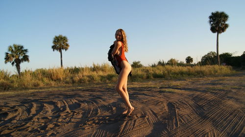 Side view full length of young woman wearing one piece swimsuit standing on sand