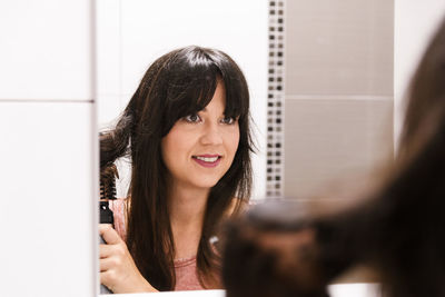 Young woman doing her hair in front of bathroom mirror.