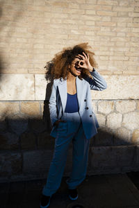 Young woman gesturing ok sign while standing against wall