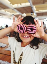 Portrait of cute smiling girl covering face donuts
