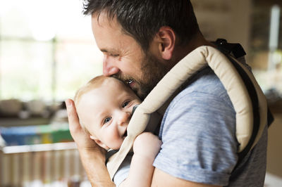 Happy father with baby in baby carrier at home