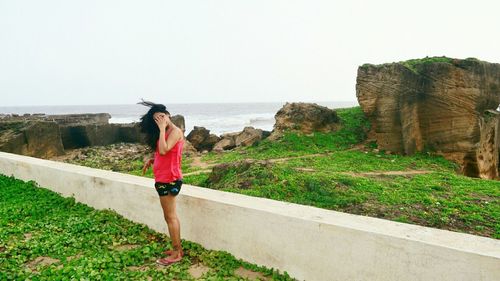 Full length of woman standing at beach by rocks against clear sky