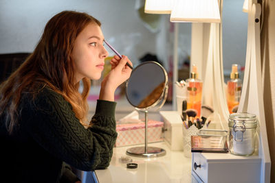 Young woman applying make-up on table