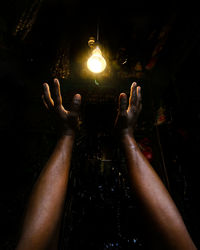 Cropped hands below illuminated light bulb