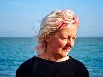 Close-up of thoughtful mature woman standing at beach against blue sky