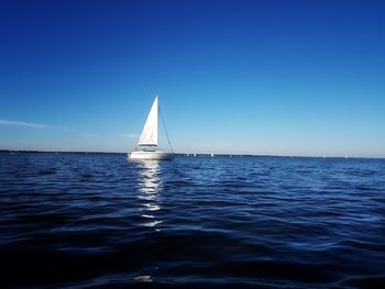 Sailboat sailing on sea against clear blue sky