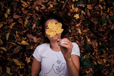Young woman holding maple leaf while lying in forest