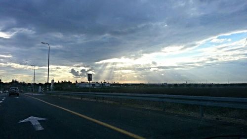 Road passing through highway against cloudy sky