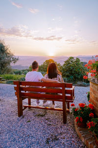 Rear view of couple sitting on bench at sunset