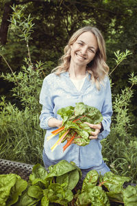 Portrait of smiling young woman holding leaf in farm