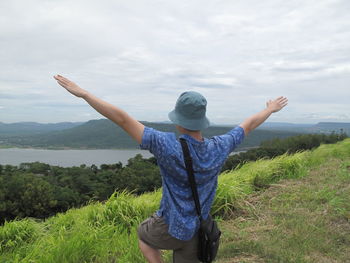 Woman with arms raised standing on landscape against sky