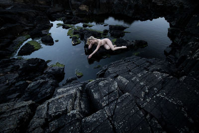 Naked woman on rock by lake against sky