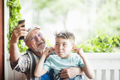 Grandfather taking selfie with grandson in porch