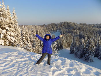 Portrait of carefree woman standing on snowfield against clear sky