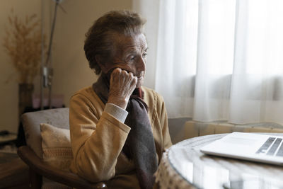 Thoughtful senior woman sitting in front of laptop at home