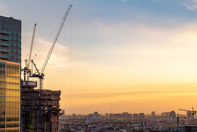 Construction site by buildings against sky during sunset