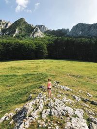 Rear view of woman standing on rock against mountain and sky