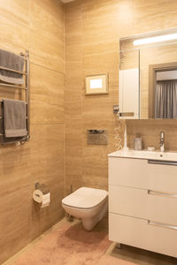 Fragment of combined bathroom in beige tones. suspended built-in toilet, heated towel rail, sink