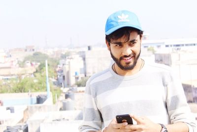 Portrait of smiling young man using mobile phone in city