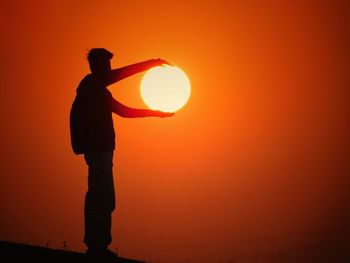 Silhouette man holding orange against sky during sunset