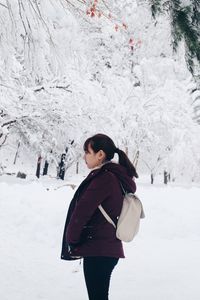 Side view of young woman standing in forest during winter