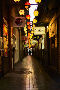 Illuminated lanterns hanging on street amidst buildings in city at night