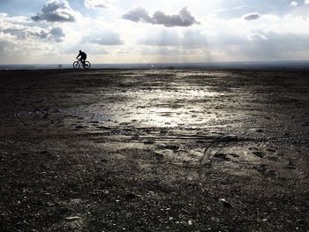 Man riding bicycle on sea shore against sky