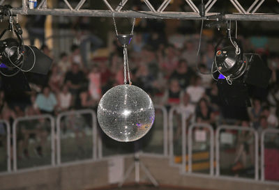 Disco ball with stage lights hanging against people sitting in auditorium