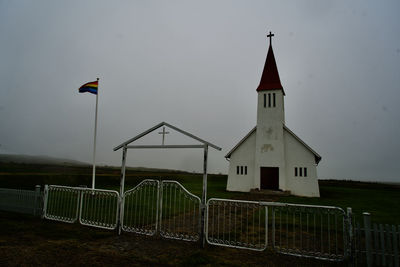 Plain church and fence with gay pride flag, against a stark grey sky, in iceland.