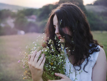 Close-up of young woman holding flowers on field