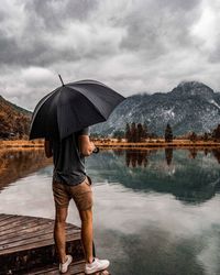 Rear view of man with umbrella standing by lake with reflection