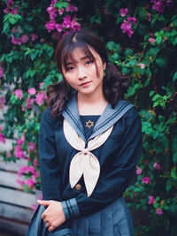 Portrait of beautiful young woman standing by flowering plants