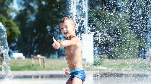 Excited boy of seven years having fun between water jets, in fountain, run around, sprinkle, have
