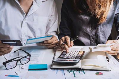 Midsection of female colleagues analyzing financial bills