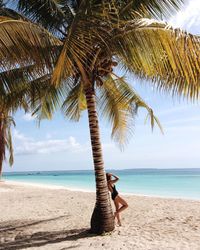 Side view of young woman in swimwear standing by palm tree at beach